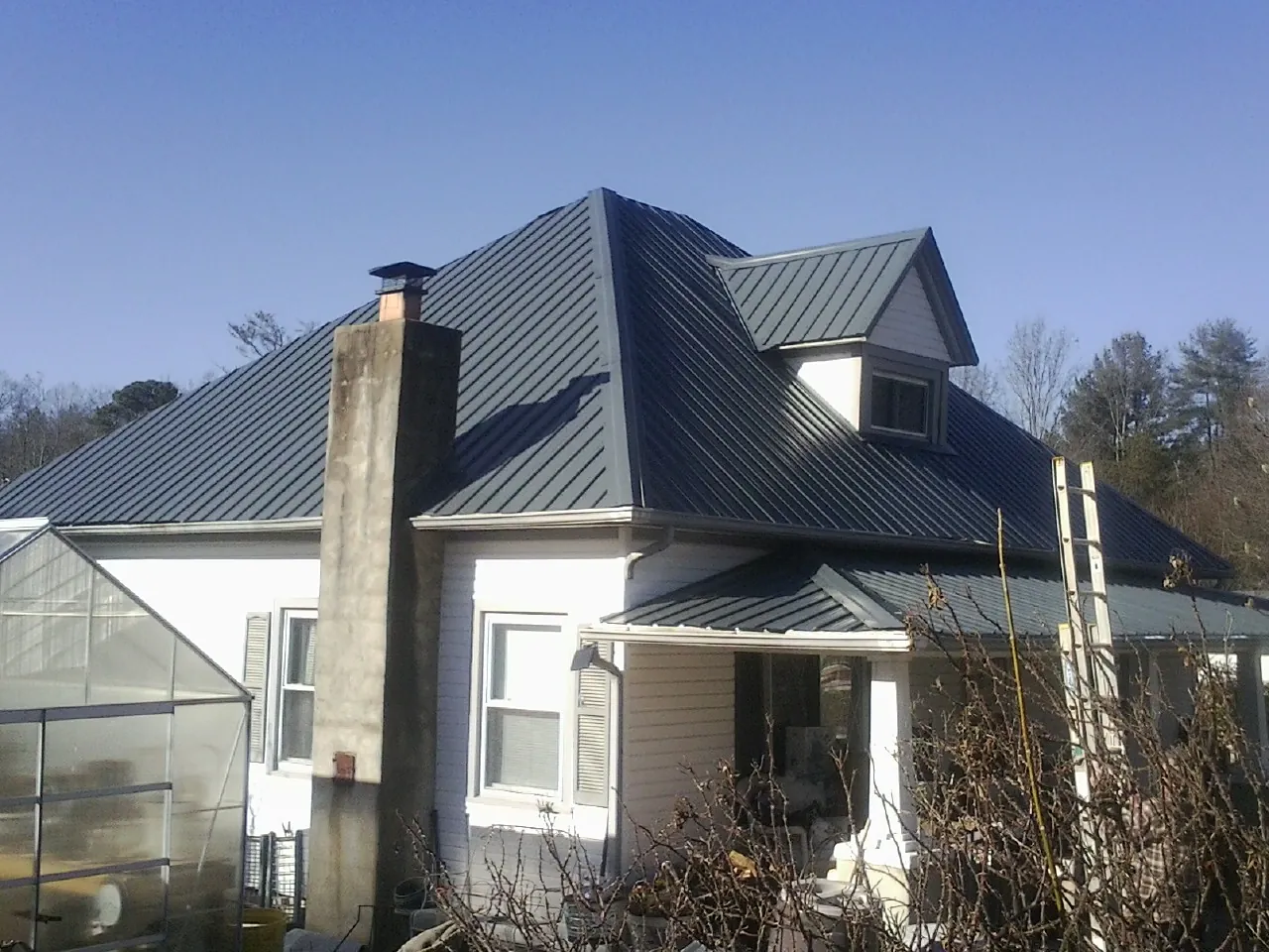 Dark blue standing seam metal roof on a white farmhouse with dormer — Slate & Tile Roof Repair by Roofing Brothers in Fergus Falls