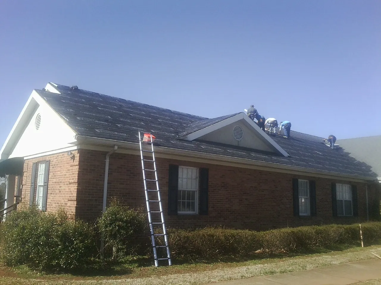 Crew tearing shingles off a brick ranch roof with a ladder set — Emergency Roof Repair work by our crew in Fergus Falls