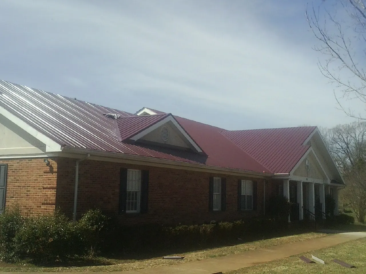 Red metal roof with gabled entries on a long brick building, from a Hail Damage Roof Repair job in Fergus Falls