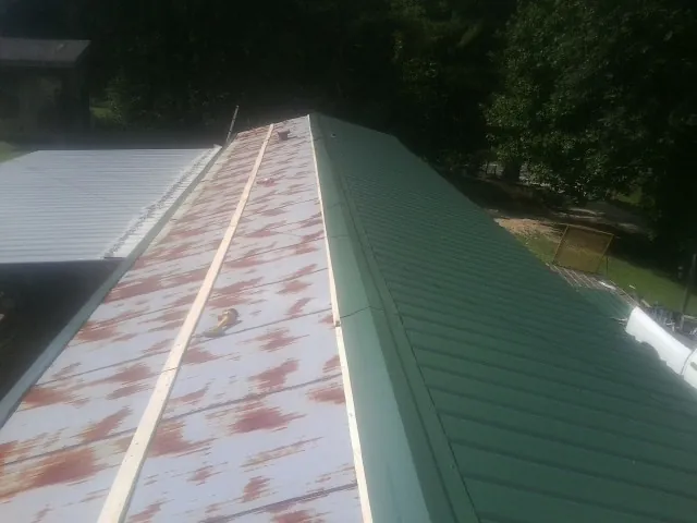 Old rusted panels beside newly installed green metal roofing — Wind Damage Roof Repair by Roofing Brothers in Fergus Falls