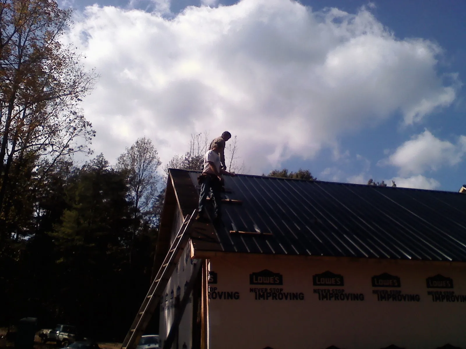 Roofer fastening dark metal panels high against a cloudy sky, from a Roof Inspection job in Fergus Falls