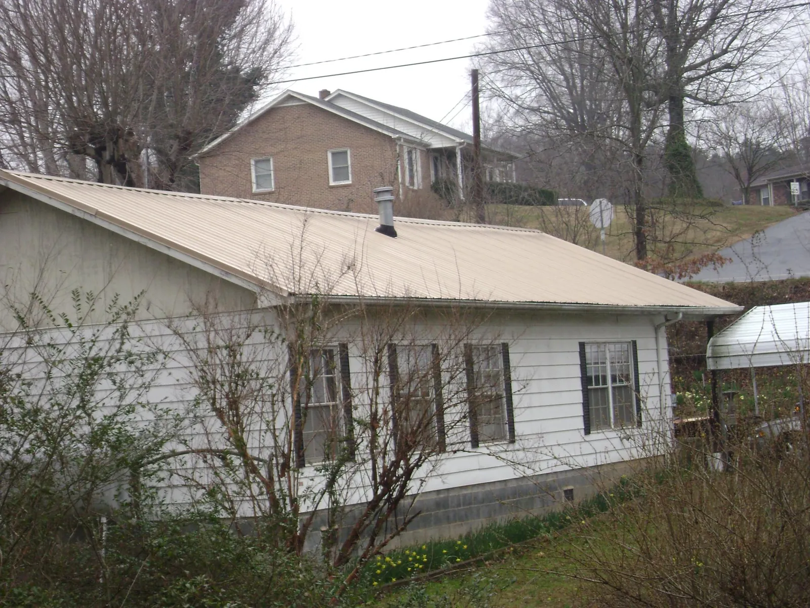 Tan metal roof on a white sided house set into a hillside — Commercial Roofing by Roofing Brothers in Fergus Falls