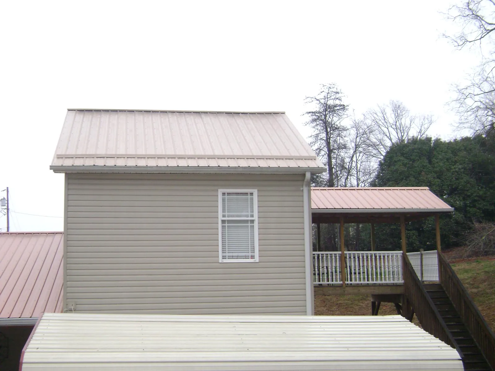 Tan metal roofs on a two story addition and attached porch, from a Roof Replacement job in Fergus Falls